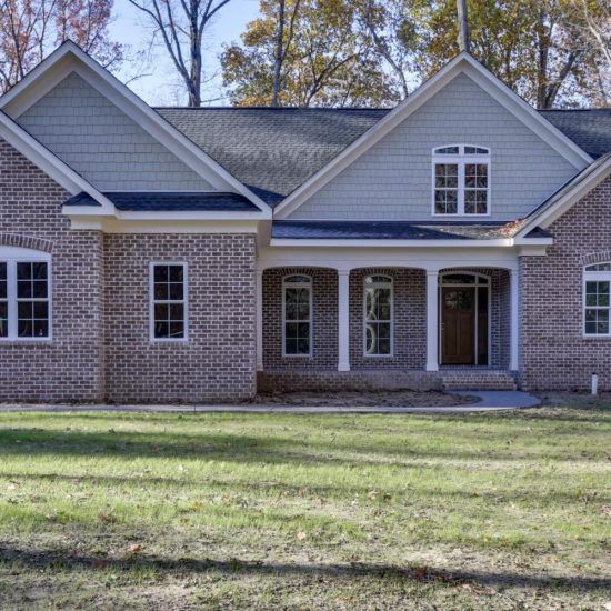 Brick suburban house with gray roof, white trim, and a front porch in a grassy yard.