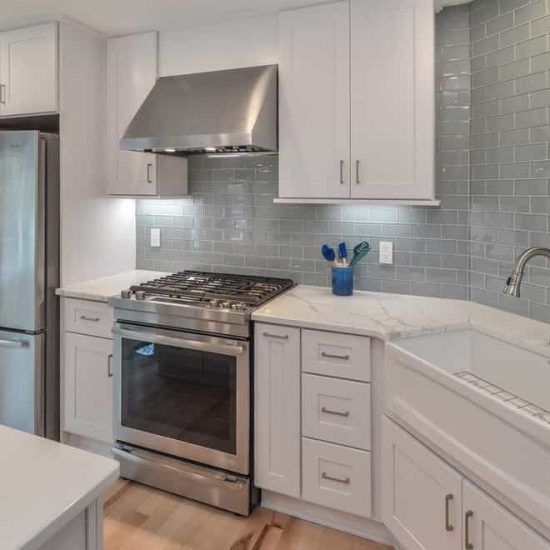 Modern white kitchen with stainless steel stove, hood, and gray tile backsplash