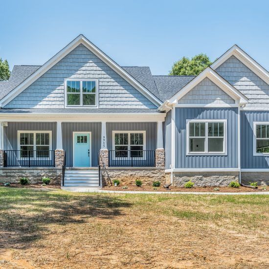 Blue-gray suburban house with white trim, a turquoise front door, and a dry front yard under a clear sky