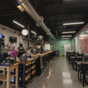 Empty café interior with a long counter, black tables and chairs, and exposed ductwork on the ceiling