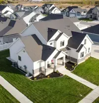 Aerial view of a suburban neighborhood with white houses, green lawns, and intersecting sidewalks.