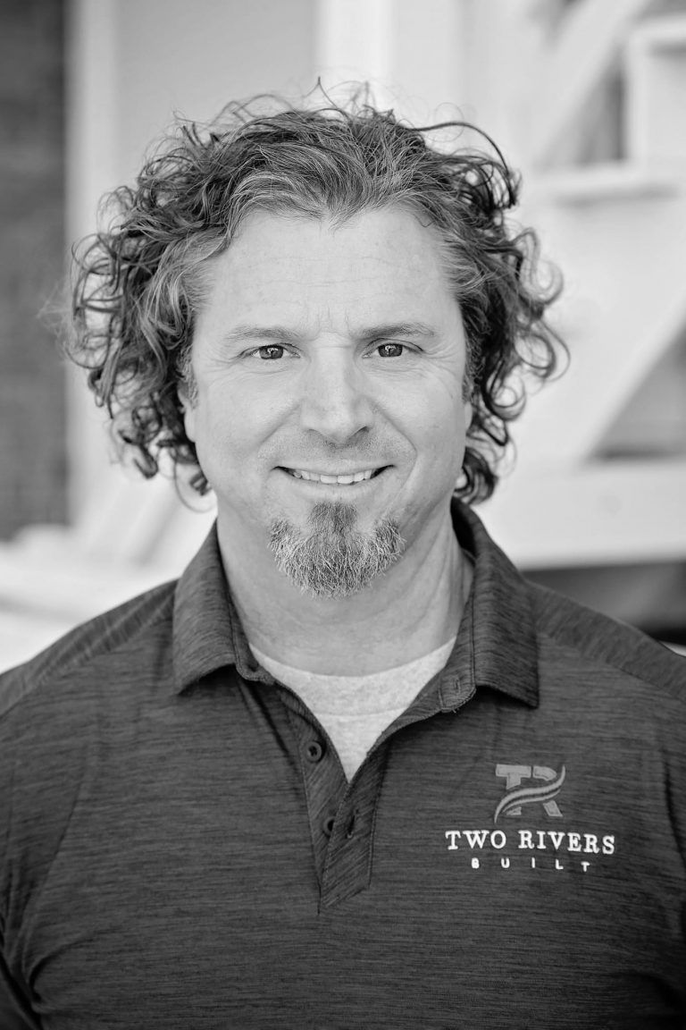 Portrait of a smiling person with curly hair wearing a dark polo shirt indoors
