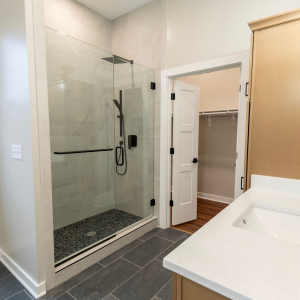 Bright bathroom with glass shower, dark tile floor, white vanity, and open closet door