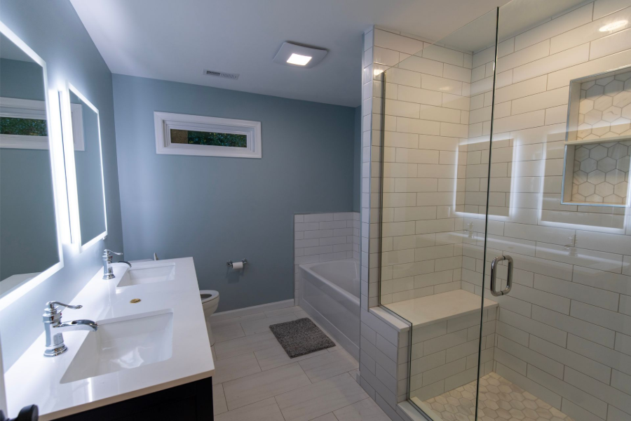 Modern bathroom with a double vanity, large mirror, tiled shower, and light blue walls.