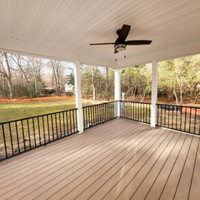 Covered porch with wicker dining chairs, glass table, potted plants, and ceiling fan in bright sunlight