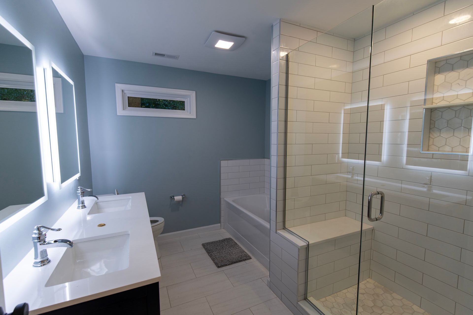Modern bathroom with double sink, glass shower, and white tile walls