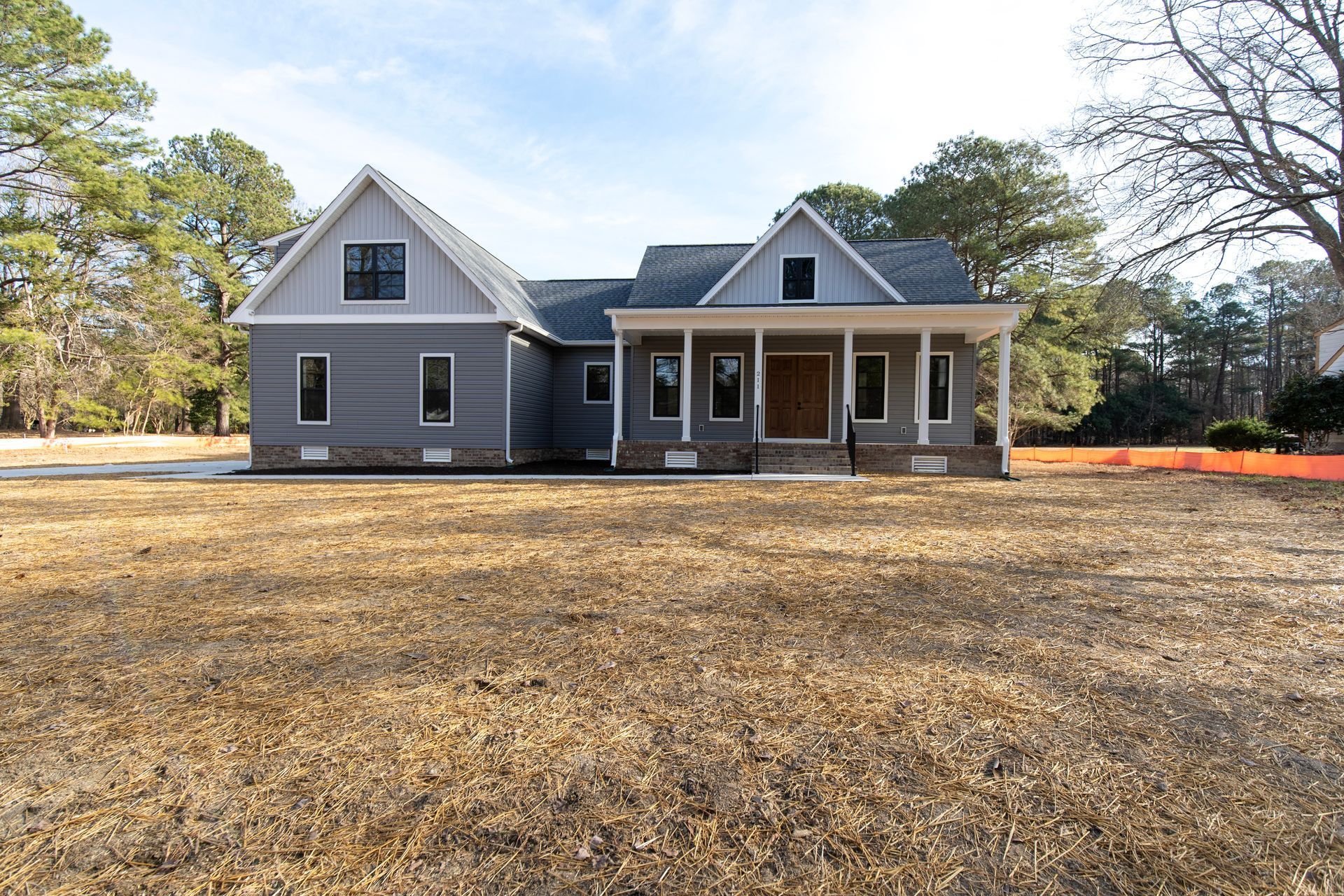 Gray house with white trim and front porch on a large bare yard under a clear sky
