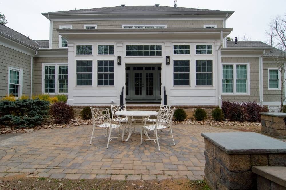 Patio with white metal table and chairs in front of a large gray house with white trim and windows