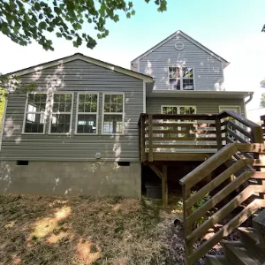 Gray house exterior with raised deck, wooden stairs, and trees overhead