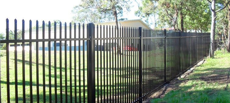 A tall, black metal picket fence stretches across a grassy lawn with trees in the background.