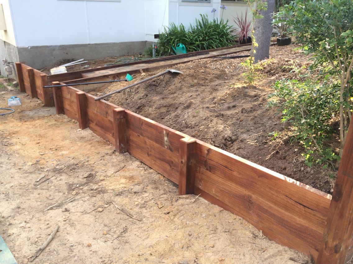 A freshly built wooden retaining wall in a backyard with soil backfill against a house foundation.