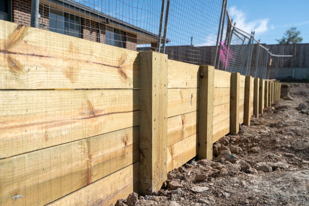 A long retaining wall made of stacked, light-colored pressure-treated wooden sleepers and vertical support posts.