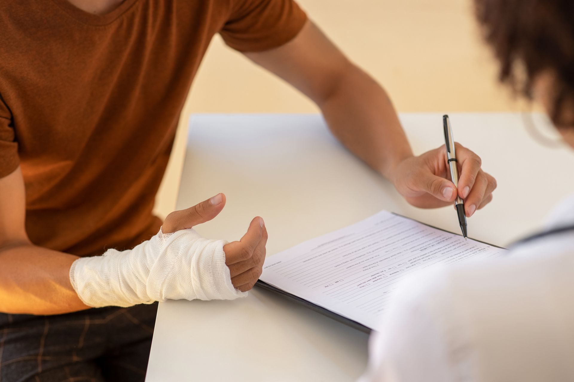 Person with bandaged wrist consults with a doctor, filling out paperwork.