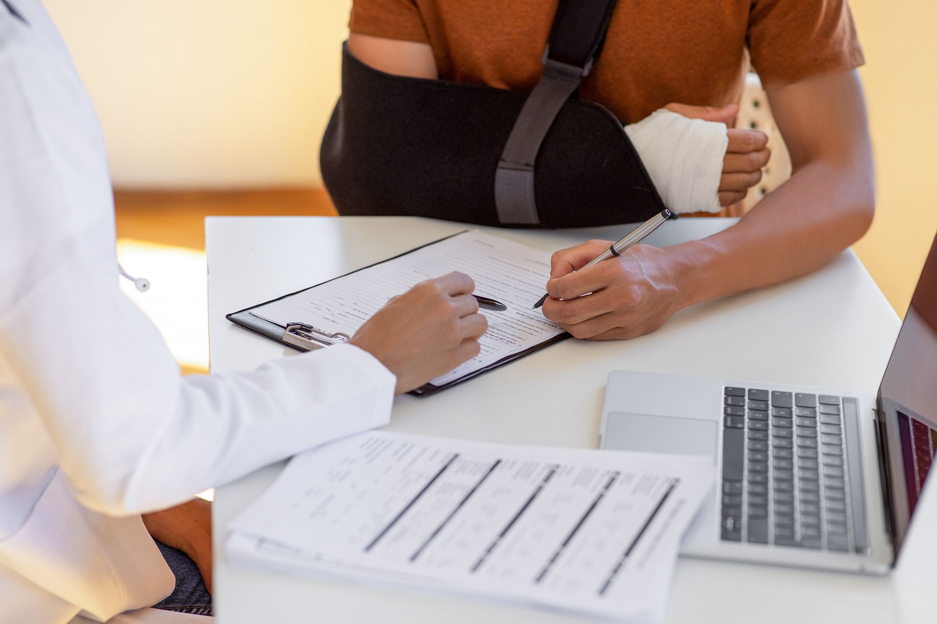 Patient with arm in sling filling out medical forms at a desk.