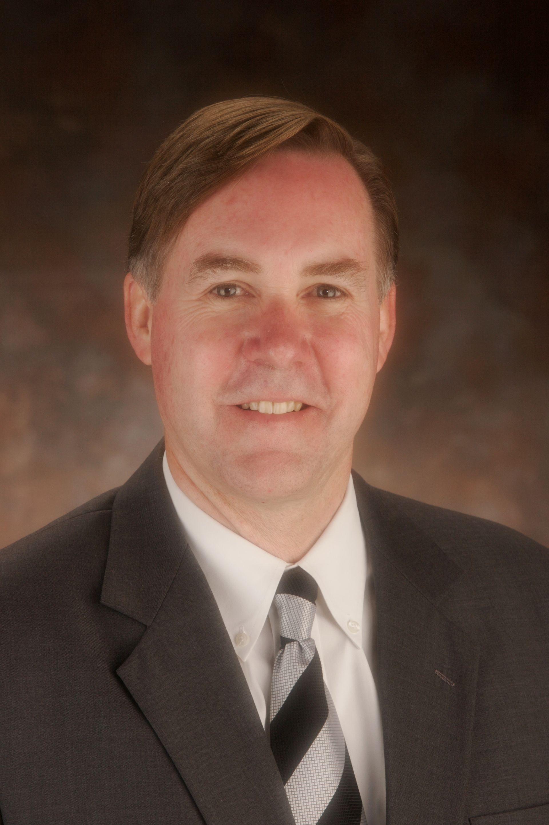Man in suit smiles at the camera; black and white striped tie.