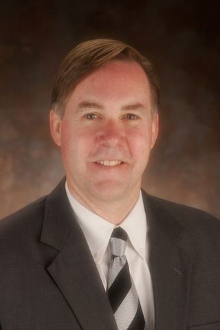Man in suit smiles at the camera; black and white striped tie.
