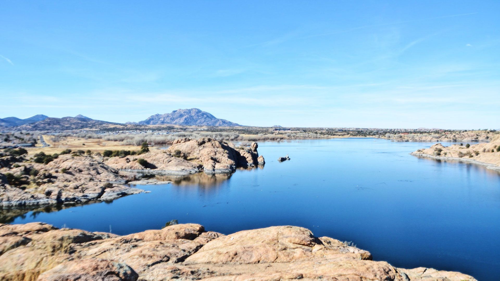 Lake surrounded by rocky terrain and a mountain under a clear blue sky.