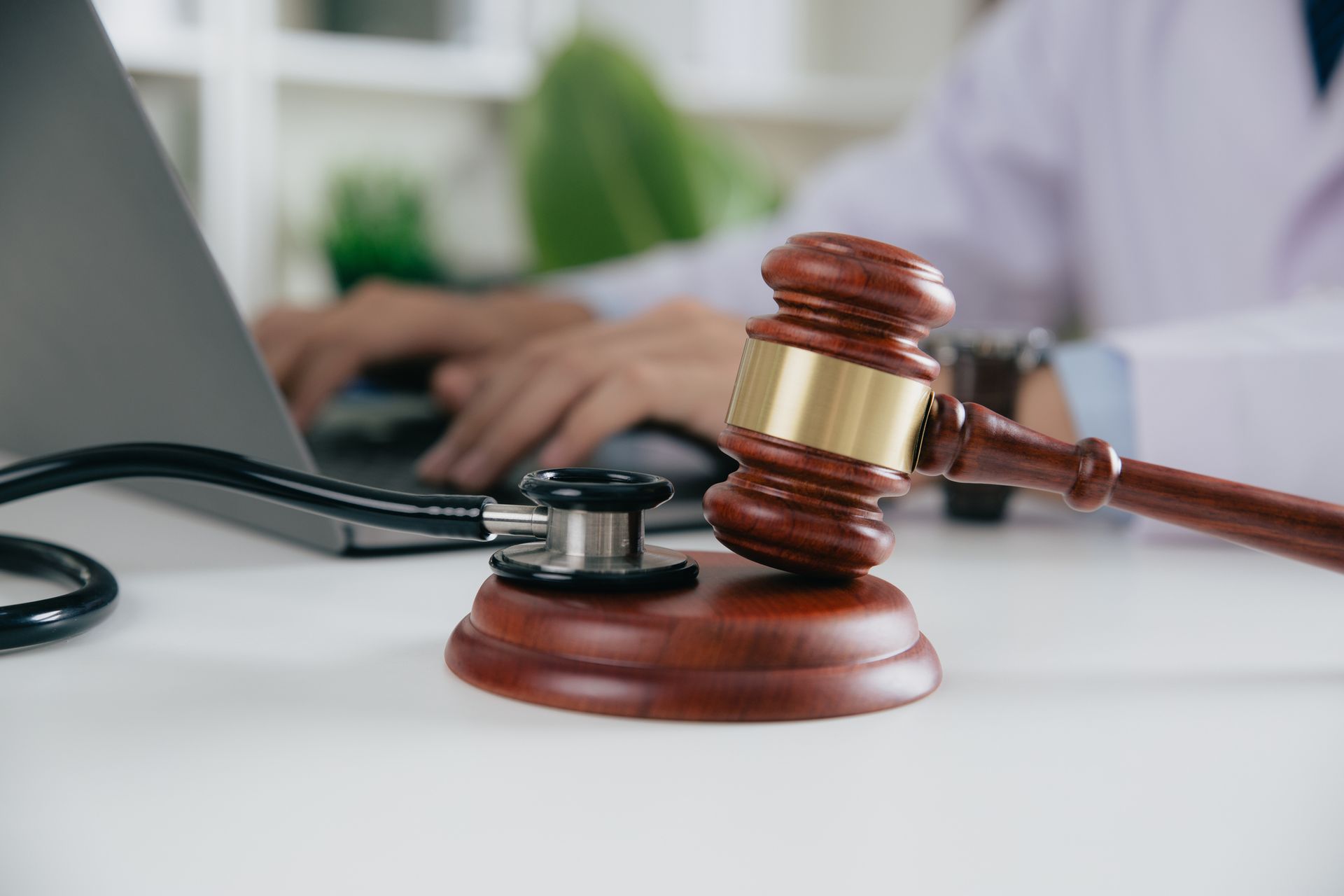 Medical expert typing on laptop with gavel, stethoscope—legal and healthcare concept at desk.