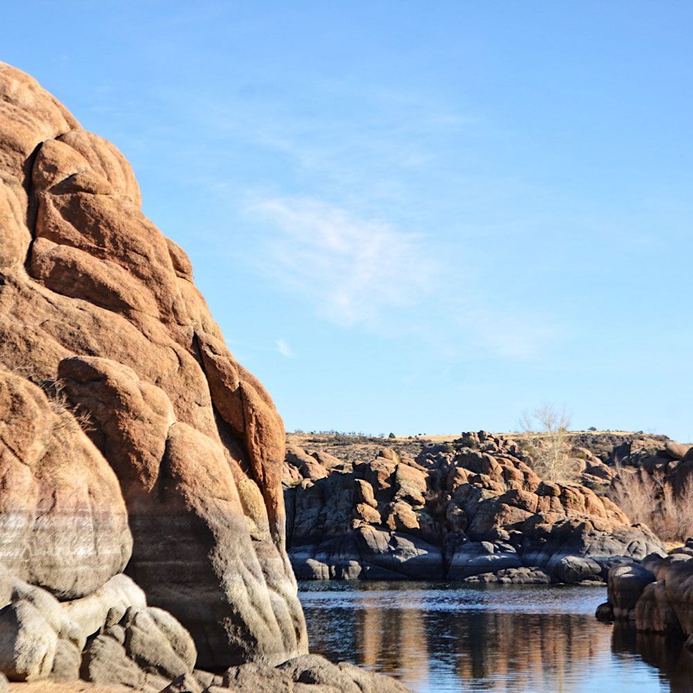Rocky shoreline beside calm water under a blue sky.