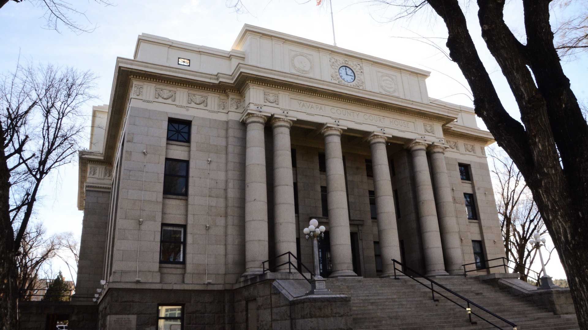 Beige stone courthouse with large columns, steps, and bare trees.