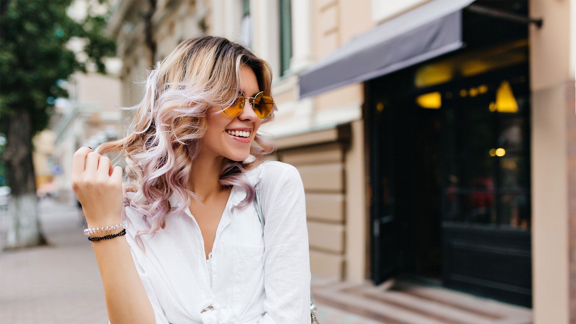 A woman wearing sunglasses and a white shirt is walking down the street.