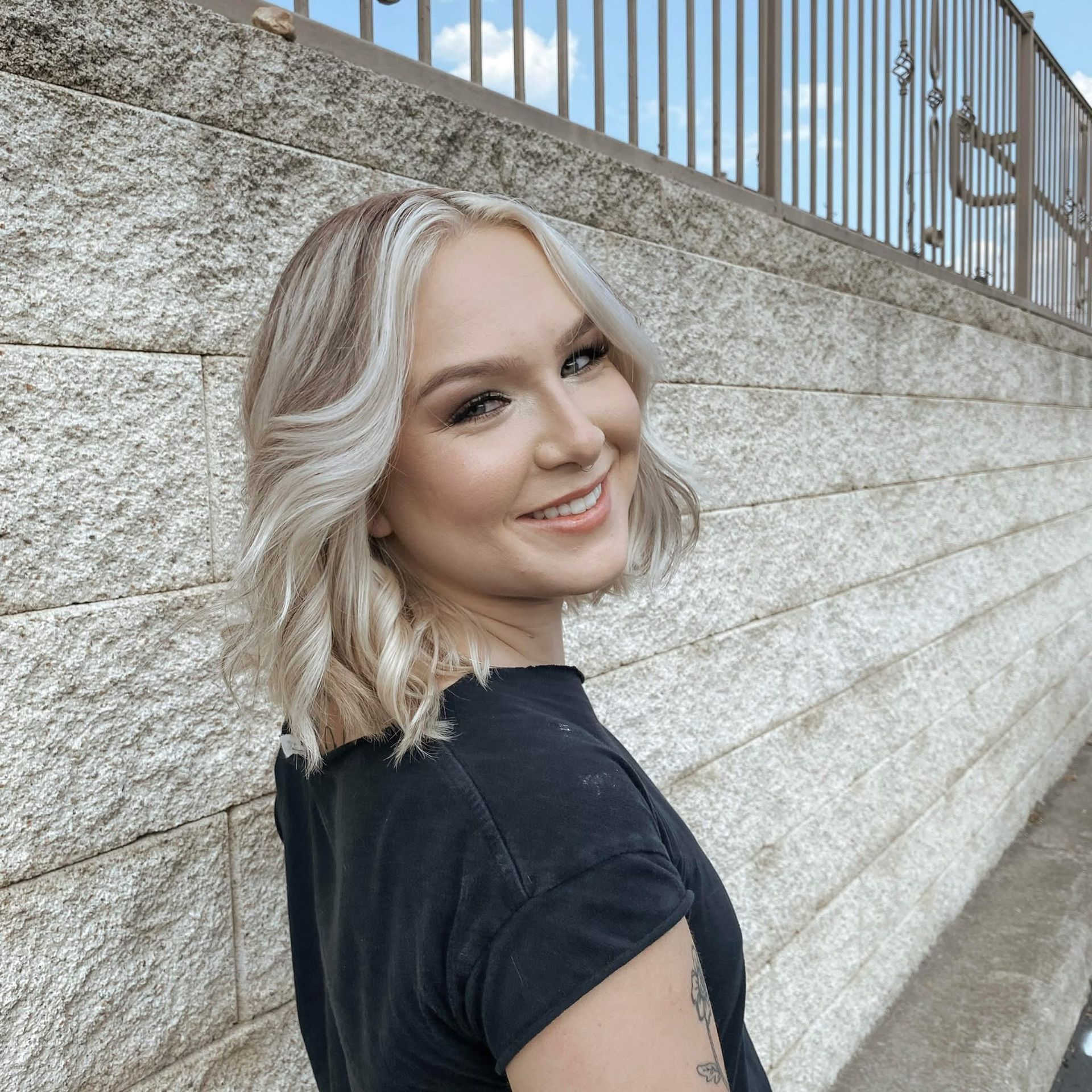 A woman in a black shirt is smiling in front of a brick wall.