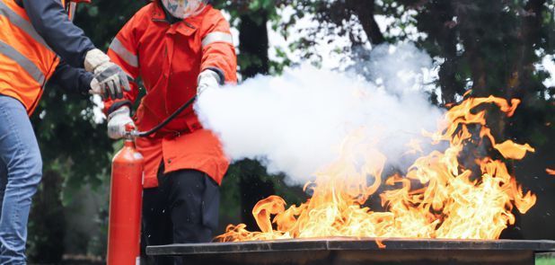 Two people are using a fire extinguisher to put out a fire.