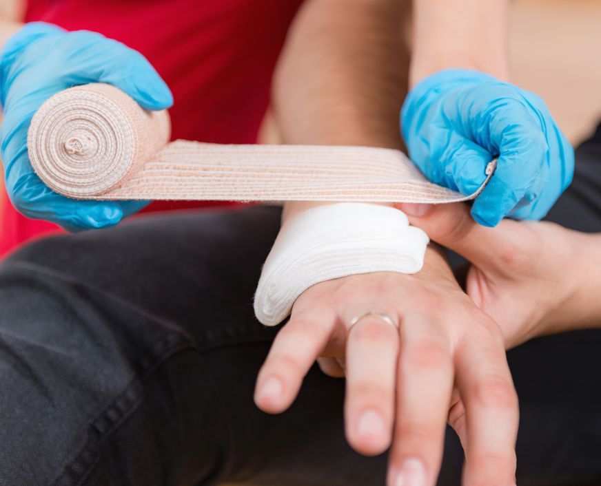 A person is wrapping another person 's hand with a bandage.
