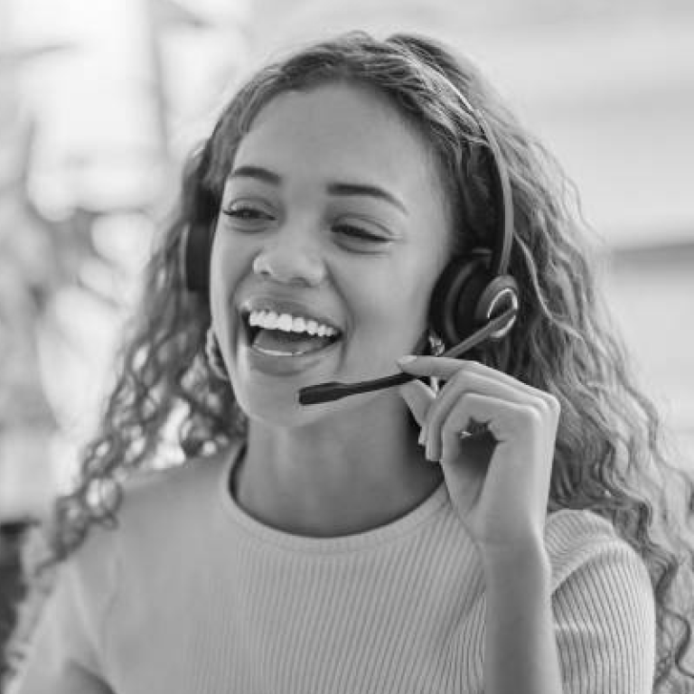 Smiling woman wearing a headset microphone, speaking on a call in grayscale.