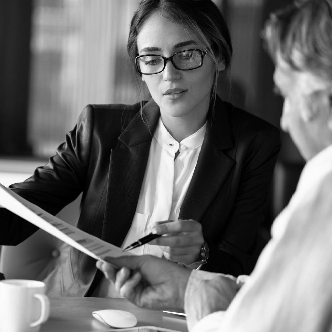 Two people reviewing documents during a meeting at a desk, one holding a pen.