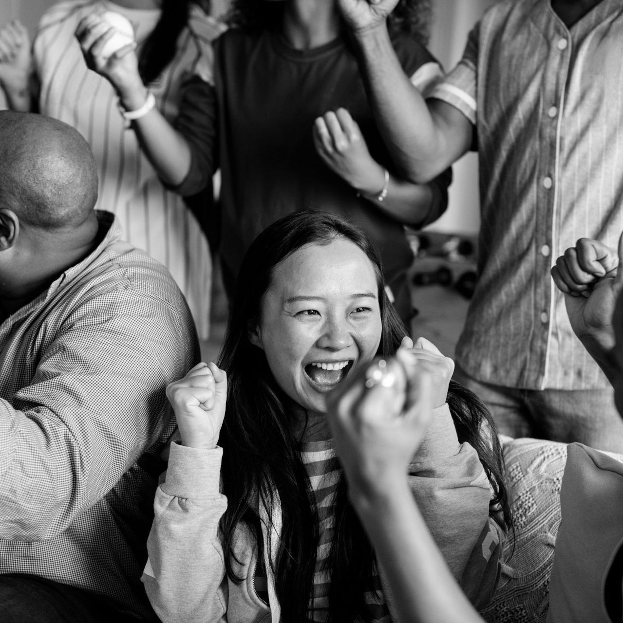 Smiling woman cheering among a crowd with raised fists in a black-and-white scene