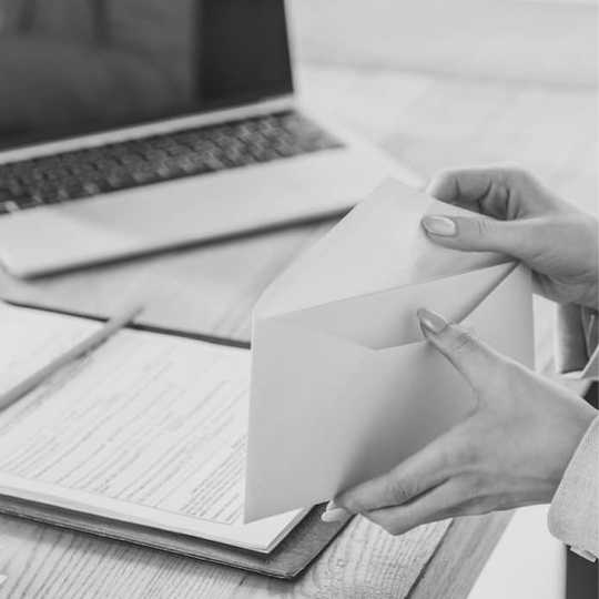 Hands opening an envelope beside a clipboard and laptop on a desk.