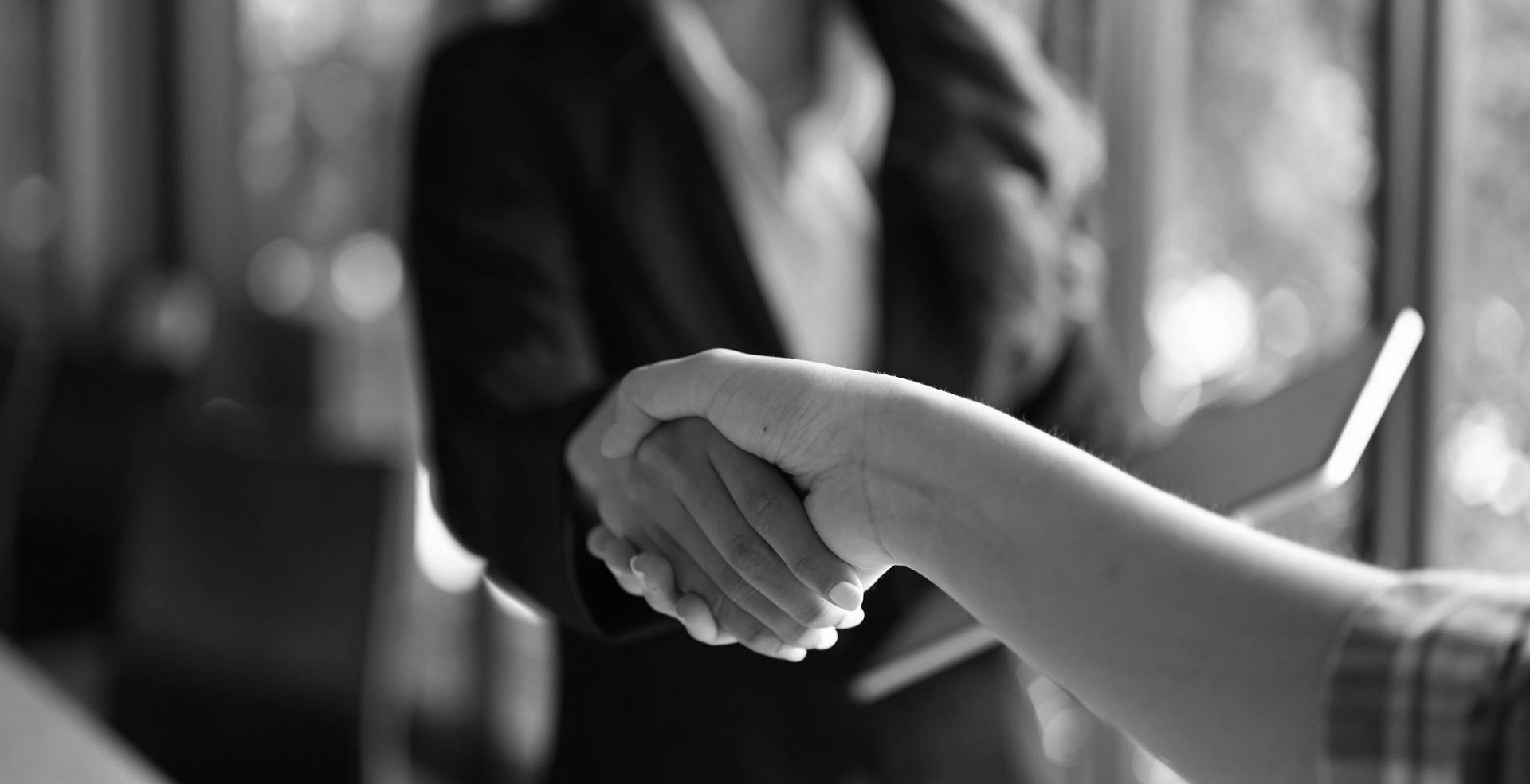 Two people shaking hands in a black-and-white office setting.