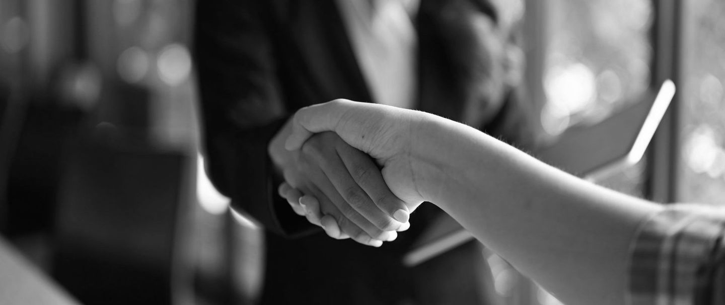 Black-and-white close-up of two people shaking hands in a business setting