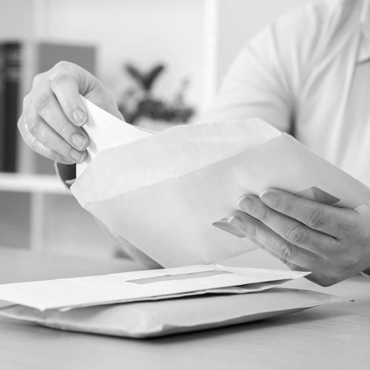 Hands opening a white envelope over stacked letters on a desk