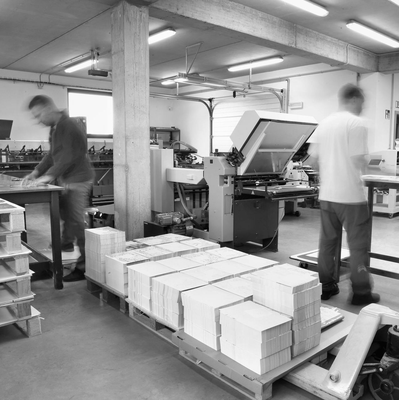 Workers in a printing facility moving stacks of paper beside a large press machine