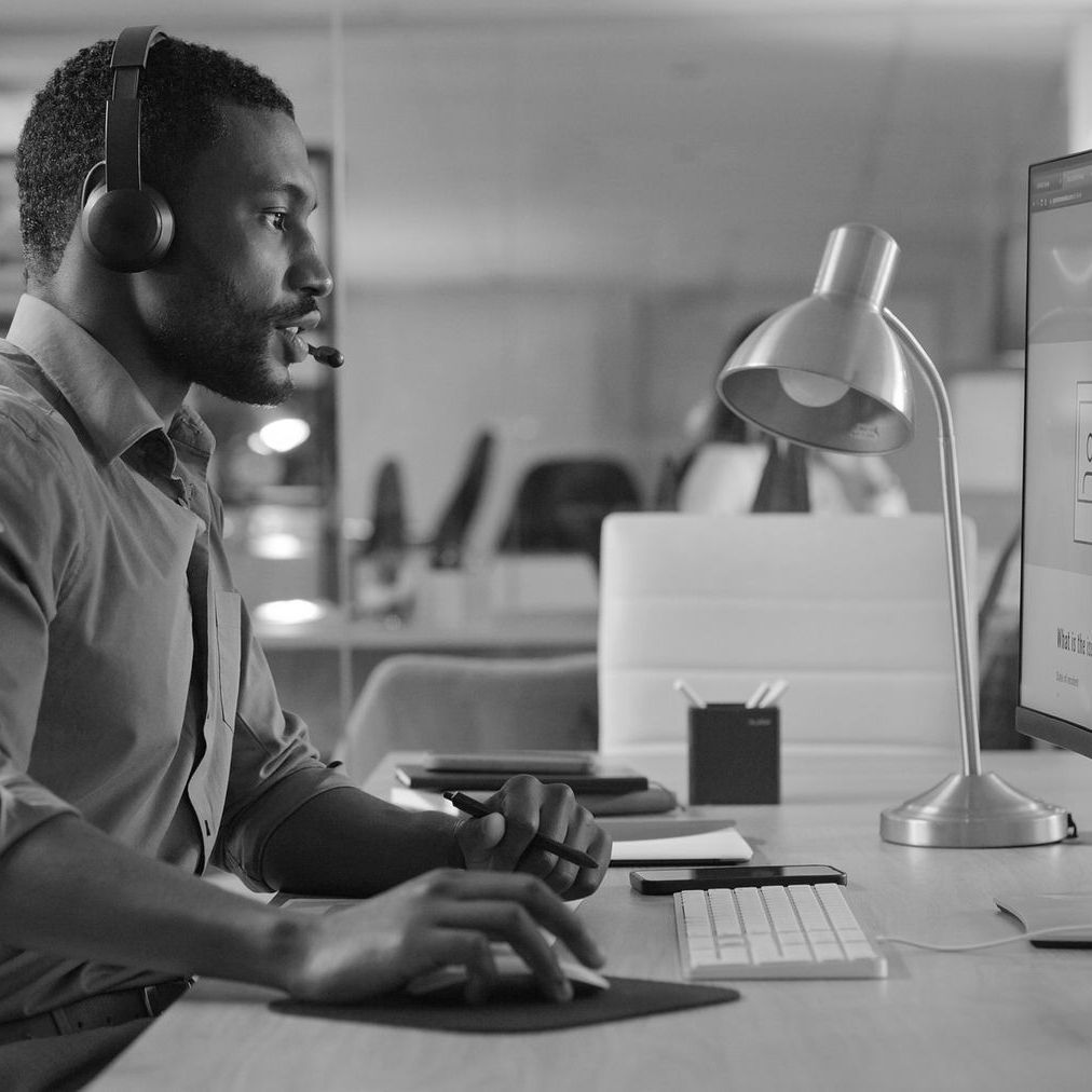 Man wearing headphones working at a desk with computer and lamp in a modern office