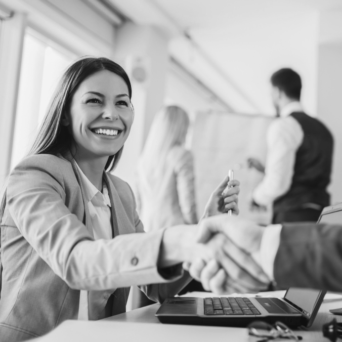 Smiling businesswoman shaking hands across a desk in a bright office