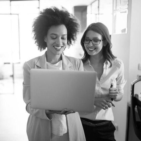 Two coworkers smiling at a laptop in an office hallway