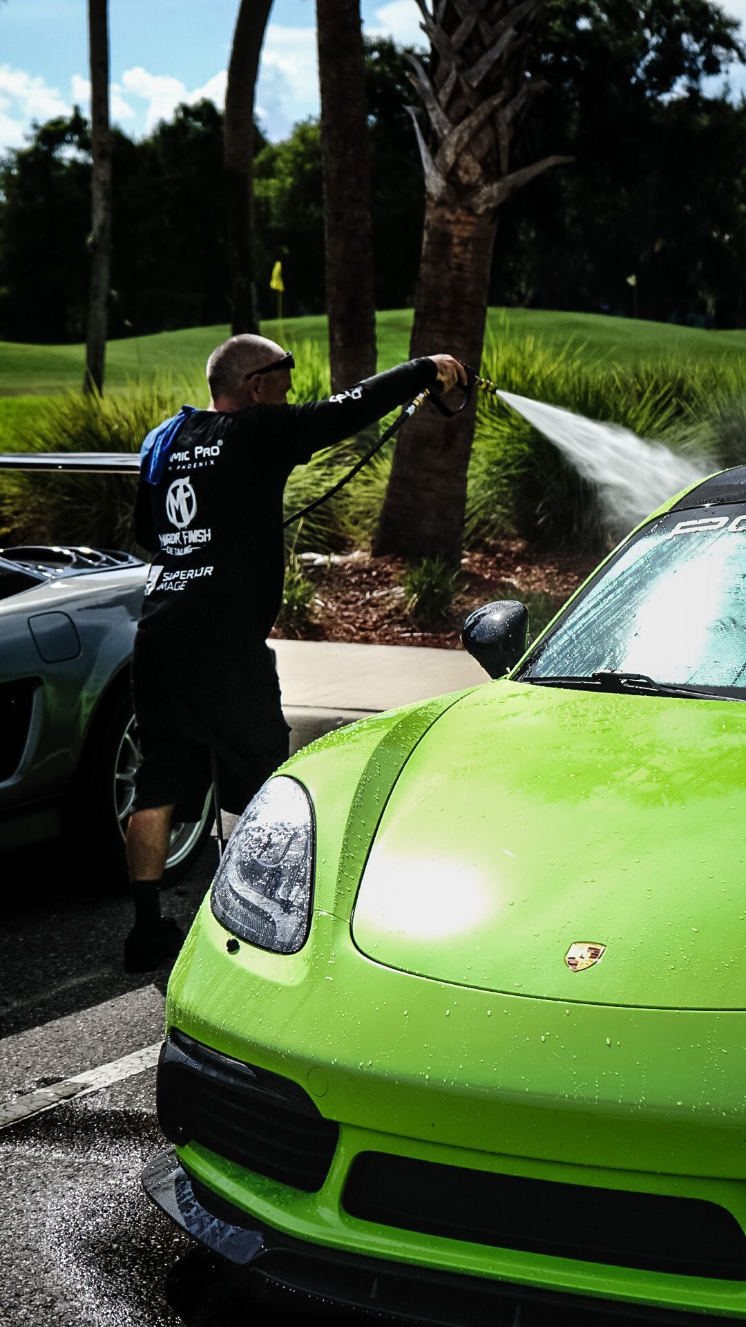 Man washing a bright green sports car with water in a sunny outdoor setting.