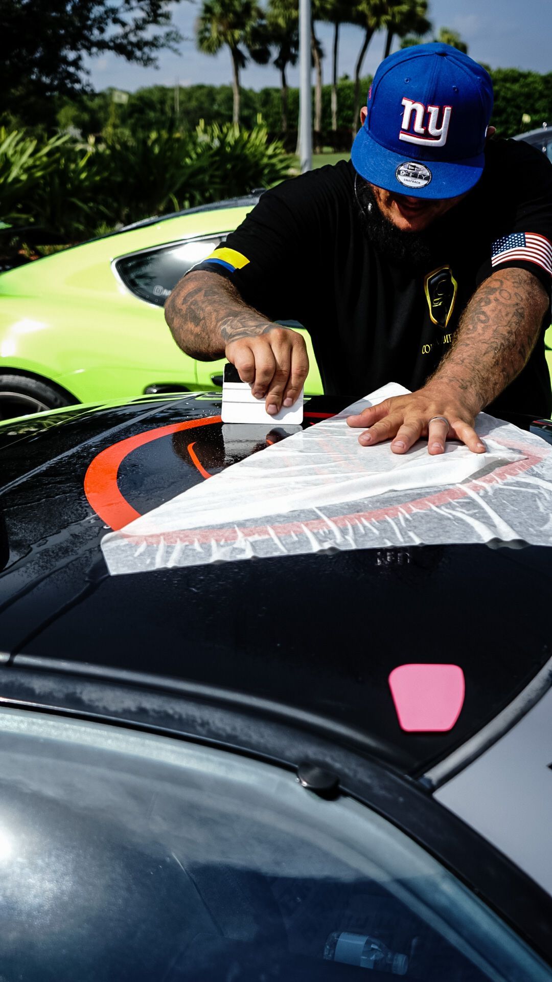 Man applying decal to car hood; wearing NY Giants hat and black shirt.