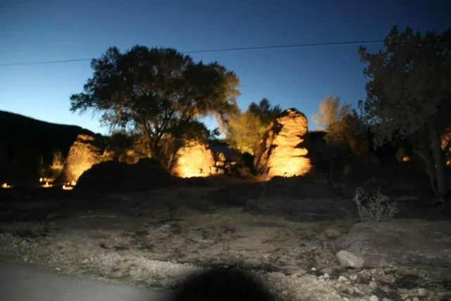 Illuminated rock formations and trees at twilight under a deep blue sky.