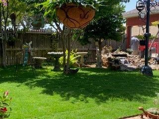 Lush green backyard garden with a hanging planter, birdbath, small waterfall feature, and a paved patio area.