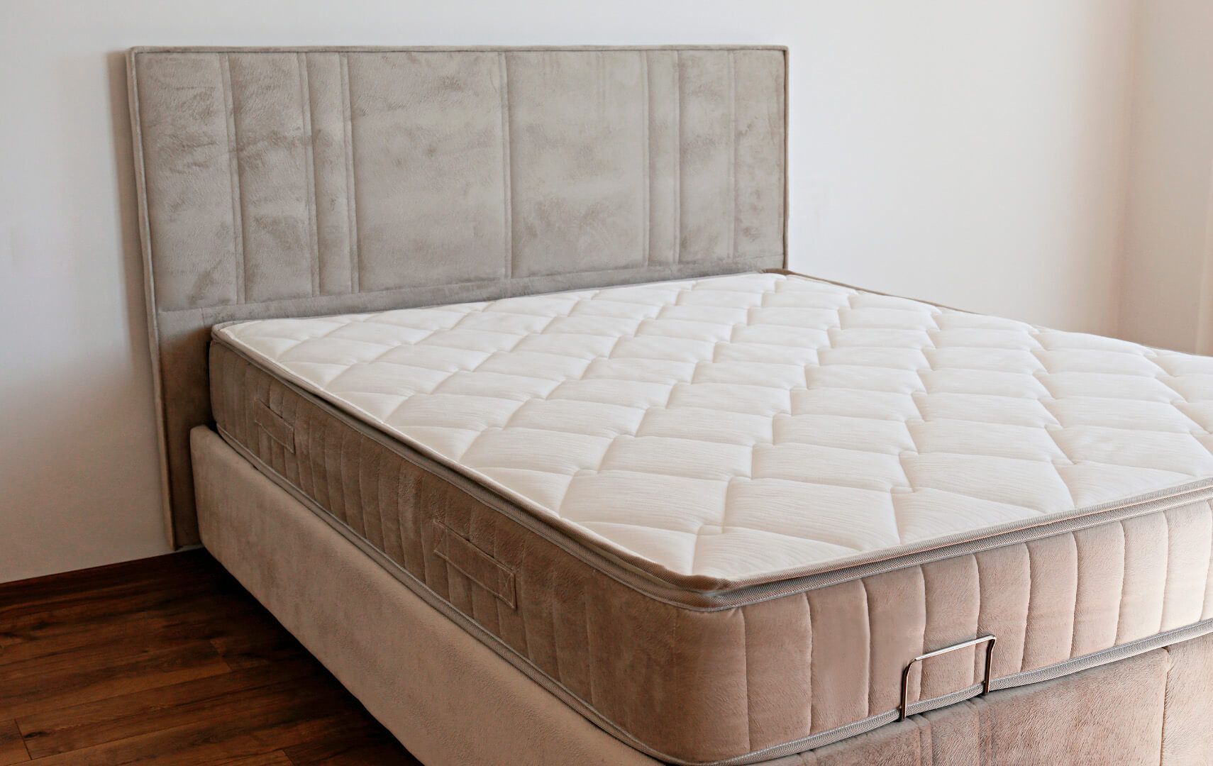 Una cama tapizada en color beige con un cabecero alto con paneles y un colchón acolchado blanco