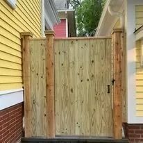 Wooden gate in a yellow house's yard. Gate is closed. Brick foundation.