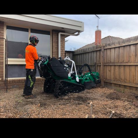 A man is standing next to a stump grinder in front of a house.