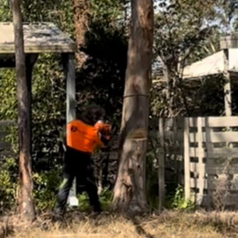A man in an orange shirt is playing paintball in the woods.
