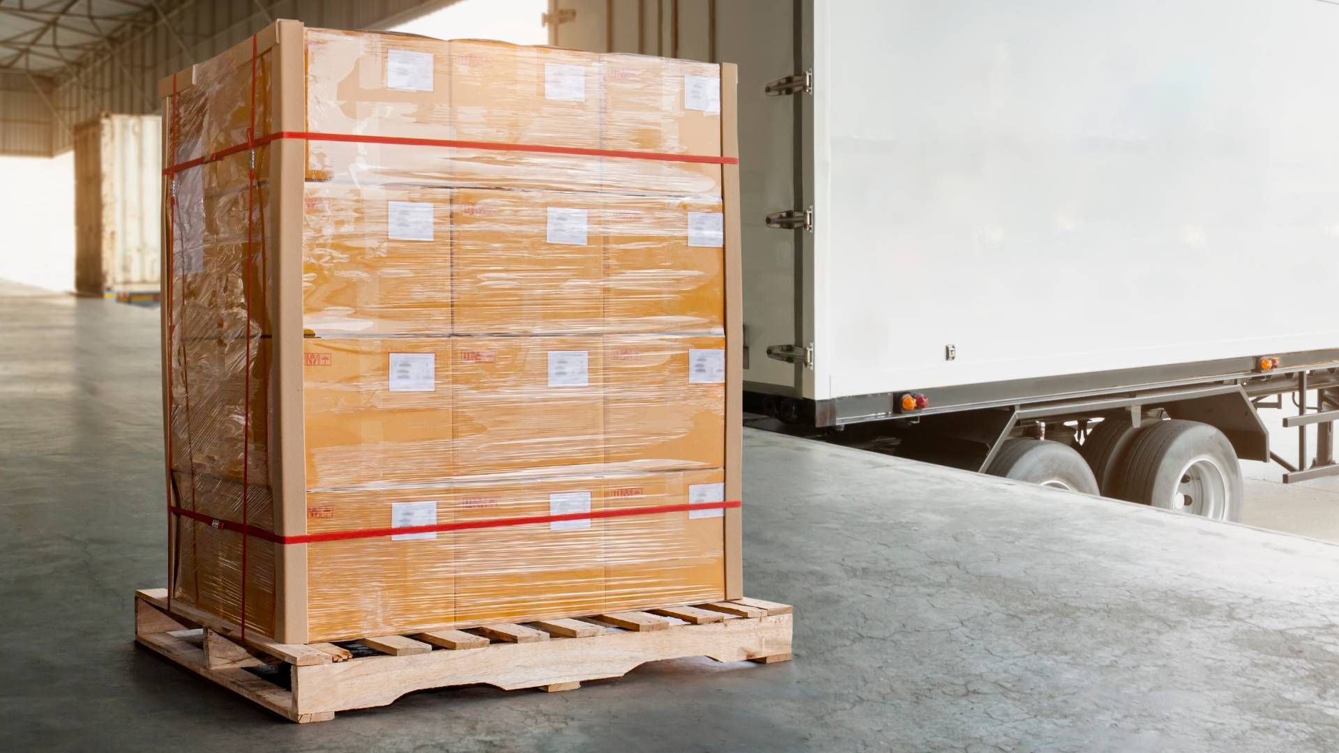 A pallet of boxes wrapped in plastic is being loaded onto a truck at a loading dock.