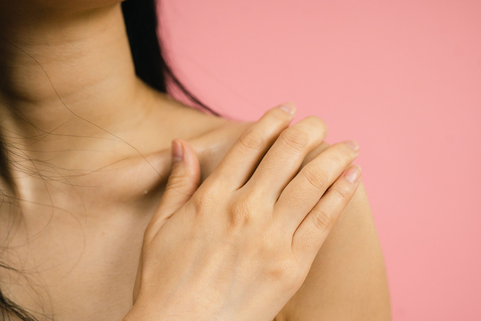 Pink background, girl in focus, touching shoulder skin exposed. 