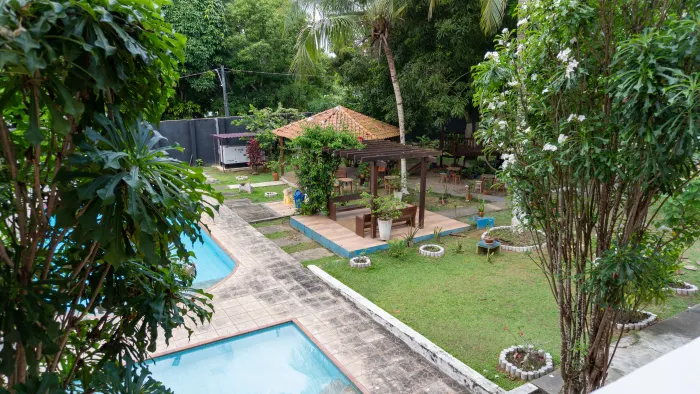 Área de piscina com gazebo em um quintal verdejante. Árvores frondosas cercam o cenário - Solar Café e Pousada